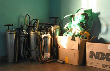 IRS spraying equipment in the corner of a green room with a brown floor and a box with equipment to the right of the image.