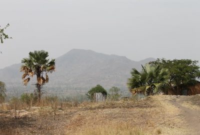 Ugandan landscape showing a dirt road, trees, house and mountain in the distance