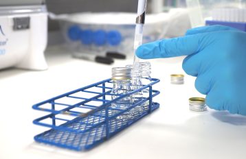 Hand in blue latex glove pipetting into clear tubes in a blue tube rack